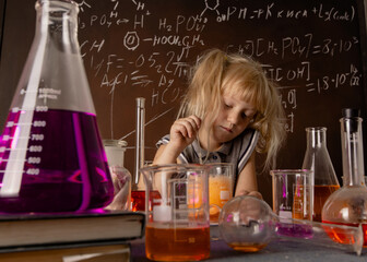 Curious little girl with test tube and colorful orange substance makes tests at school laboratory. Small kid observes chemical reaction. Biology education concept.