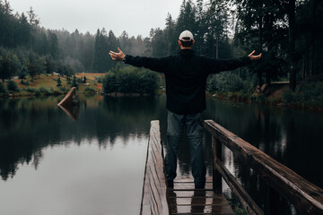 Young man standing on loodgate pond in rainy weather. Natural reserve Czech canada, dark mood green