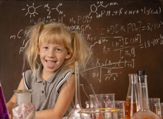 Curious little girl with test tubes and colorful substances making tests anf keeping her toungue ou at school laboratory. Small kid learning chemistry and conducts science experiment on biology lesson