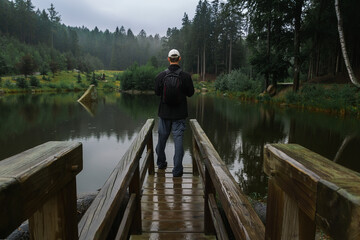 Young man standing on loodgate pond in rainy weather. Natural reserve Czech canada, dark mood green