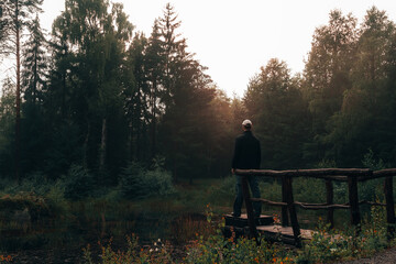 Young man standing on pond floodgate in sunset. Natural reserve Czech canada, dark mood green