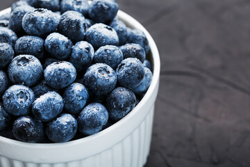 Blueberries in a white Cup on a black textured background.