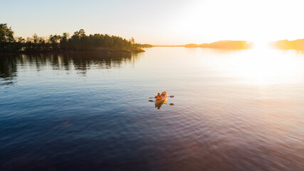 Mother with a child floats on a red kayak in the middle of a large lake in the rays of a beautiful summer sunset, aerial view