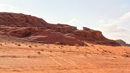 Rocky massifs on red sand desert, bright cloudy sky in background - typical scenery in Wadi Rum,...