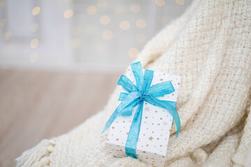 gift box with turquoise ribbon, lying on cozy chair covered with a soft blanket