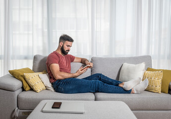 Obraz premium Young beautiful man or guy lying on the sofa at home reading the book and enjoying his free time without his wife and children with smile and happy face