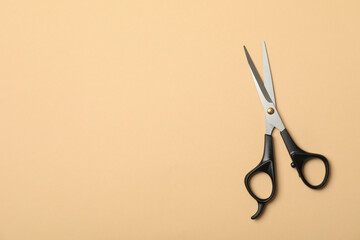 Black hairdresser scissors on beige background, space for text