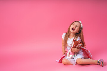 Little cute smiling girl with bow on her head, hugging her favorite handmade toy