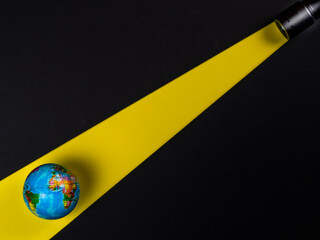 Flashlight illuminating a globe with a yellow beam of light on a black background.
