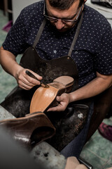 Obraz premium Male cobbler sitting at his shop and repairing man's shoe, brushing glue over sole. Vintage look.