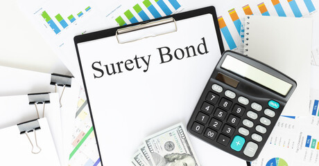 Text SURETY BOND is written on a notebook with a pen and a magnifying glass lying on the table. Business concept.