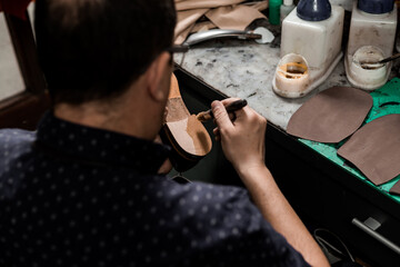 Male cobbler sitting at his shop and repairing man's shoe, brushing glue over heel.  Vintage look.