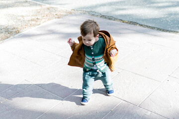 A year and a half old baby taking his first steps in a park with a loose stone floor