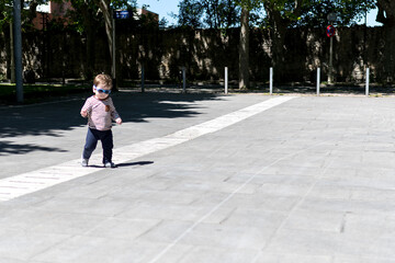 A year and a half old boy walking down the street with a pair of sunglasses on