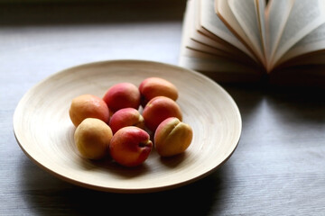 Wooden bowl with fresh apricots and open book on a table. Selective focus.