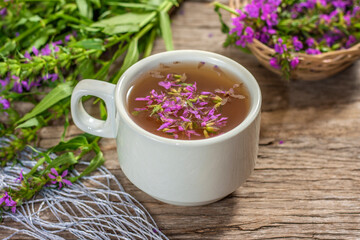 Fireweed is a healthy herbal tea. Mug of traditional russian drink ivan tea on a wooden background with fireweed flowers