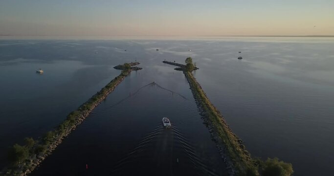 Aerial drone view of boats travelling through river canal and out onto the lake during sunset in Ontario, Canada in 4K