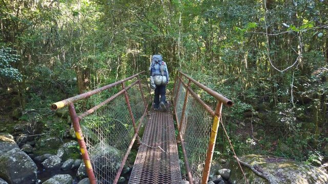 A Hiker Crosses A Small Metal Bridge In The Forest.