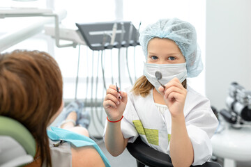 Fototapeta na wymiar Little girl switched roles with her female dentist. Caucasian child holding dental instruments in her hands