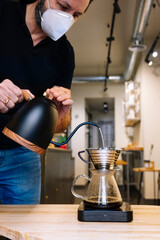 Waiter preparing coffee.Pouring milk. He wears a mask on his face.