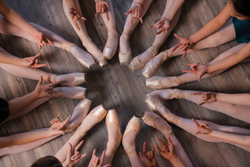 Ballet school students in ballet shoes sit on the floor
