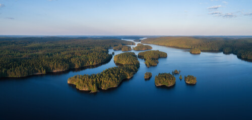 Aerial panorama of beautiful blue lake, islands and green summer forest in Finland. Blue sky. Top view. Summer sunset lanscape.