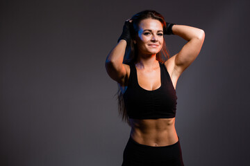 Fototapeta na wymiar Portrait of a professional fighter and boxer girl who straightens her hair showing her pumped up abs on a dark background
