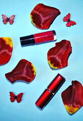 Fashion background with red tulip petals, lipstick, raspberry-red nail polish and wooden butterflies against light-blue background. Flat lay. Beauty. Concept for 8 March, Valentine, Mother' day