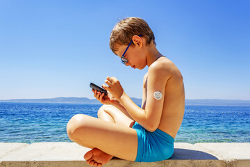Diabetes. Summer sea holidays: a boy sitting in a Lotus position on the beach measuring sugar...
