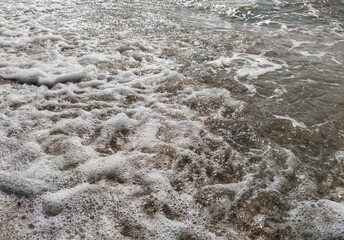 Foamy, bubbling, large sea waves close-up mixed with sand.