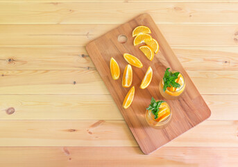 Cold summer orange lemonade in glasses and fresh oranges near on wooden table. Top view with copy space.