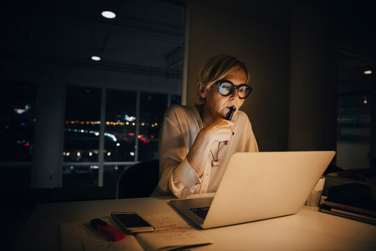 Thoughtful businesswoman looking at laptop while working late in creative office - Powered by Adobe