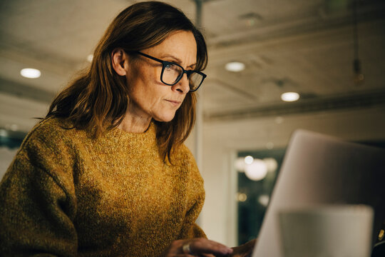 Determined mature female entrepreneur working late while using laptop at workplace