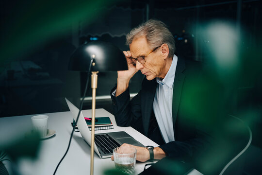 Worried senior businessman working late while sitting with laptop at coworking space
