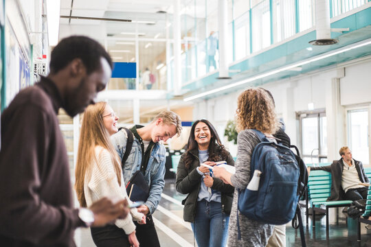 Cheerful young male and female students talking while standing in cafeteria at university