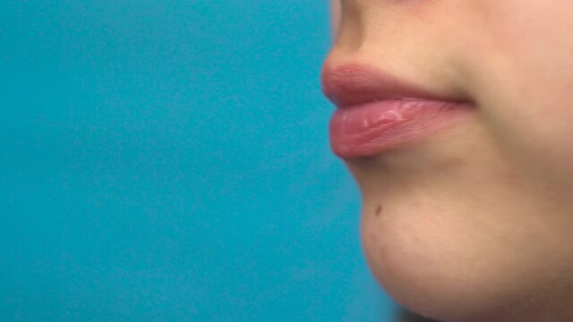 Teenager girl with braces on her teeth eats a red apple on a blue background. Girl with colored braces bites off an apple closeup.