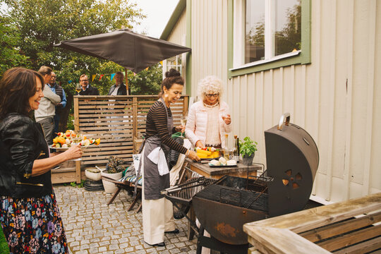 Smiling senior women preparing dinner on barbecue grill at back yard