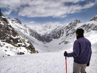 Manali, India - June 14th 2019: Hiker enjoying an epic panoramic mountain top view of Spiti Valley under snow in the month of June from top of Indian Himalayan peak on a Humpta pass Trek near Manali.