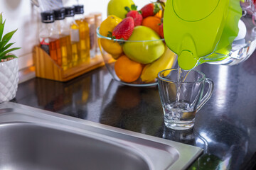 Pouring filtered water into glass from jug in the kitchen