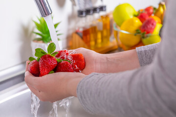 Woman washing strawberries in the kitchen - Powered by Adobe