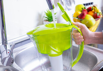 Woman filling water filter jug in the kitchen