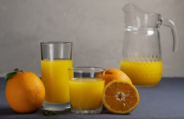 Orange juice in different glasses and a jug with oranges on a gray background