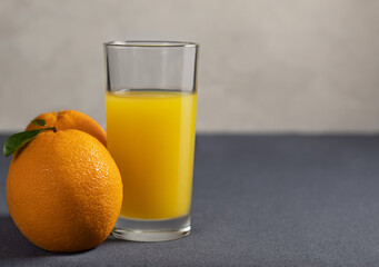 Orange juice and oranges on a gray background.