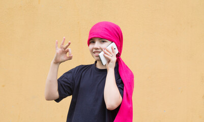 girl with cancer and head scarf using mobile phone  and making an ok sign