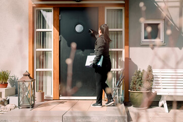 Young delivery woman with package at entrance of house