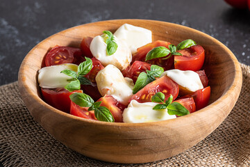 Homemade caprese salad in wooden bowl on black background close up. Traditional Italian dish.