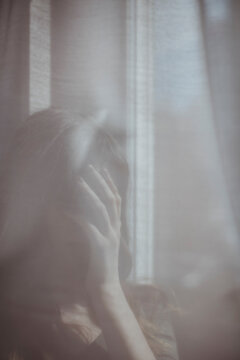 Young woman hiding behind white window curtain