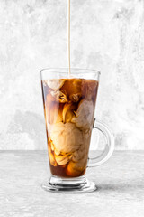 Milk pouring into a glass of iced coffee