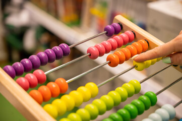 Closeup female hand calculating with balls on wooden rainbow abacus for number calculation. The concept of learning arithmetic for preschoolers.