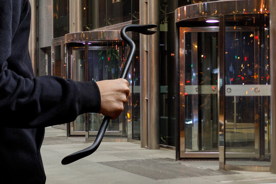 Thief With A Burglar Tool In His Hands At The Entrance Of The Store Door.